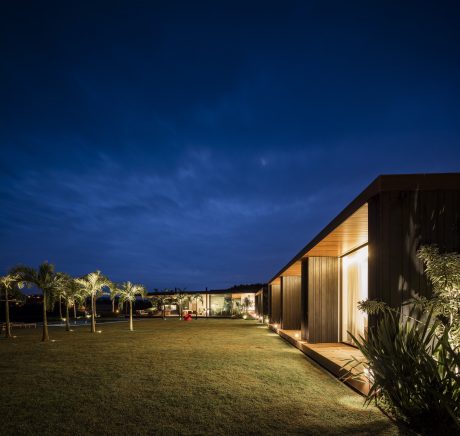Sleek modern building with warm lighting, surrounded by lush tropical greenery at night.