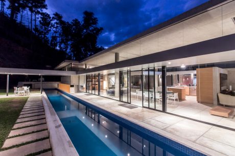 Sleek, modern home with expansive glass walls, swimming pool, and lush landscaping.