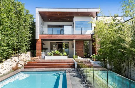 A modern two-story home with a deck, pool, and lush greenery surrounds it.