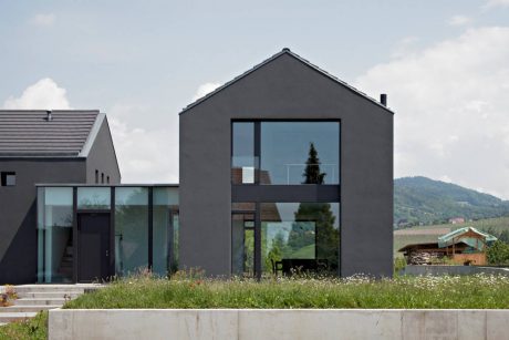 Modern, sleek architecture with large glass windows, contrasting black exterior, and lush natural surroundings.