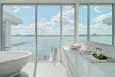 Modern bathroom with floor-to-ceiling windows overlooking a body of water and cityscape.