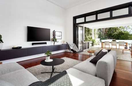 Spacious living room with minimalist black furniture, large windows, and lush greenery outside.