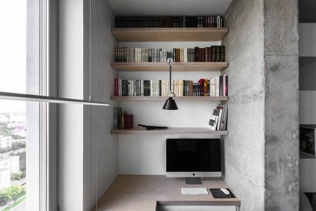 Minimalist home office with concrete walls, floating shelves, and a desk with a computer.