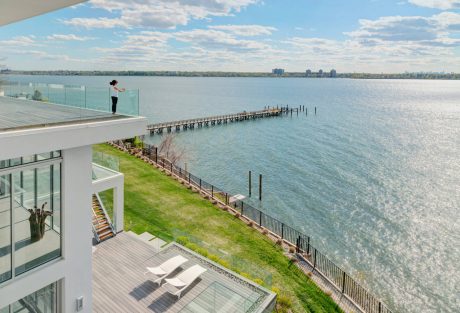 A modern, glass-enclosed structure with a balcony overlooking a scenic lake and pier.