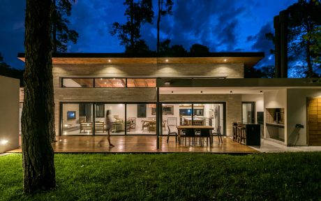 Modern home with expansive glass walls, wooden exterior, and outdoor living area.