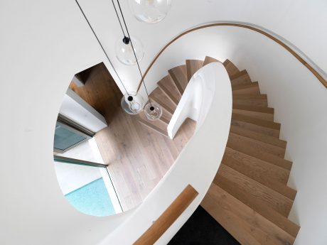 Modern spiral staircase with wood steps and glass wall, reflecting circular mirror.