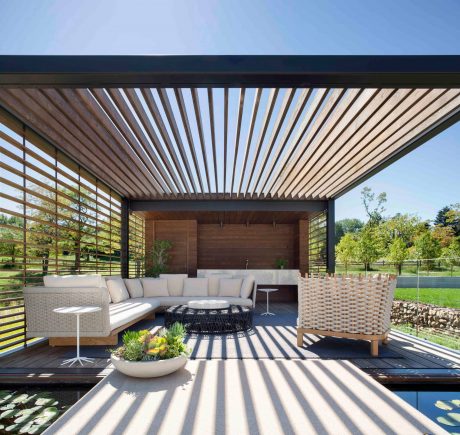 Covered deck with slatted wood canopy, woven outdoor furniture, and reflecting pool.