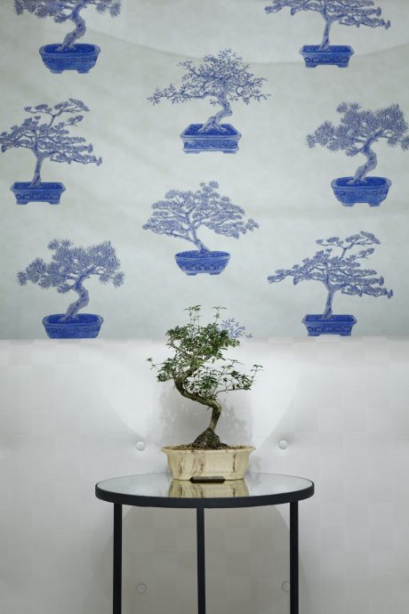 Ornate bonsai tree against a wallpaper featuring stylized blue bonsai trees.