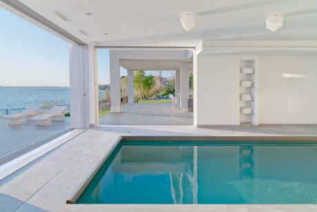 Modern indoor pool with sleek white decor, floor-to-ceiling windows, and a scenic view.