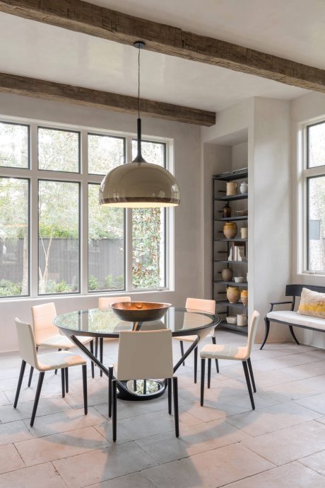 A modern dining area with exposed wooden beams, large windows, and a sleek glass-topped table.