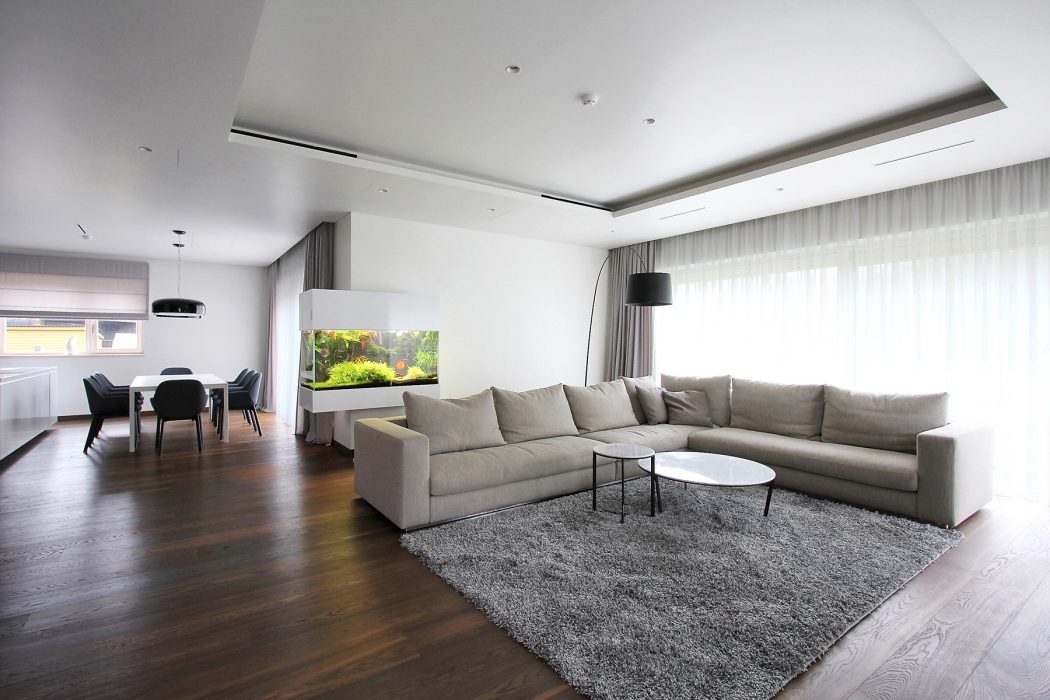 Spacious living room with modern grey couch, recessed lighting, and view of dining area.