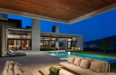 Luxurious open-concept home with sleek concrete, wood, and glass design; stunning pool.