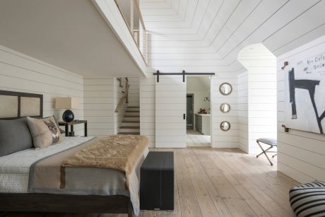 Spacious bedroom with high-ceilinged, whitewashed walls and wooden floors. Sliding barn door and stylish decor.