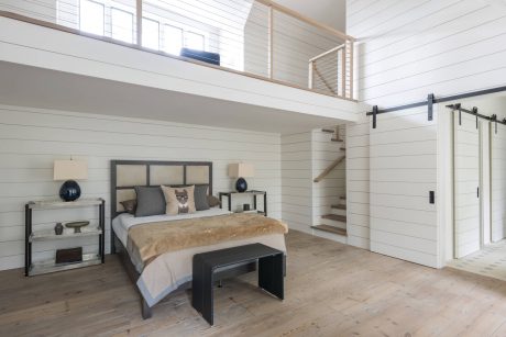 Spacious modern bedroom with high ceilings, barn door, and wood plank flooring.