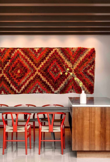 Vibrant textured wall art, modern wood furniture, and bold red chairs create an inviting ambiance.
