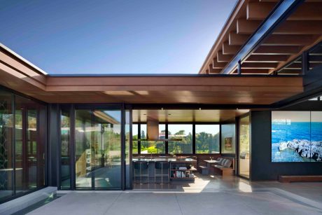 Modern open-concept interior with wood-beamed ceiling, expansive windows, and sleek furnishings.