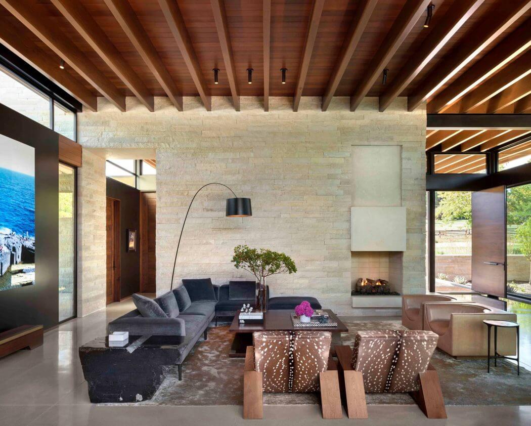 A spacious open-plan living area with a stone accent wall, wooden ceiling beams, and modern furniture.
