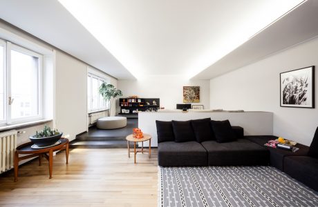 Sleek, modern living space with minimalist furniture, shelving, and large windows providing ample natural light.