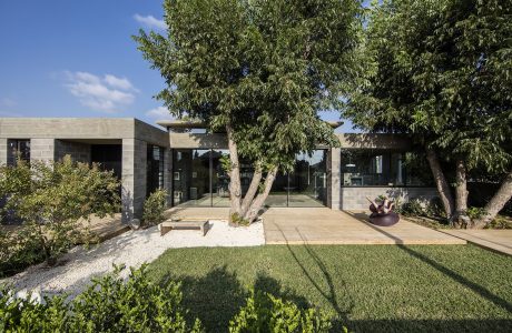 Modern concrete and glass building surrounded by lush greenery and a sculpture.