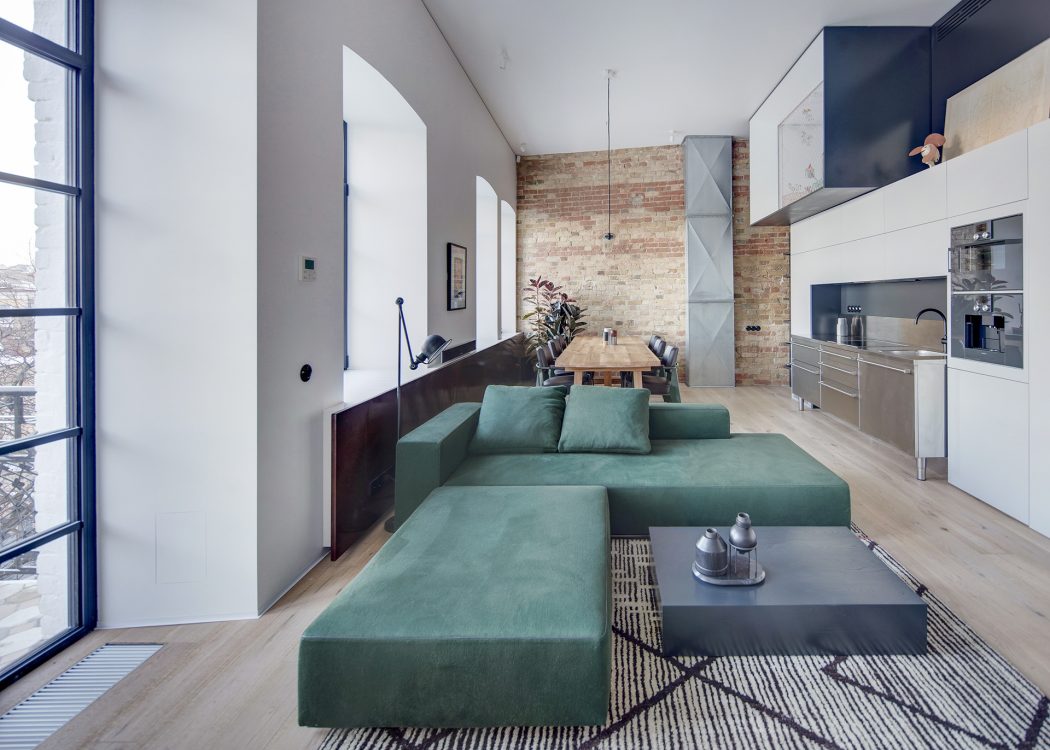 A modern, open-concept living space featuring exposed brick walls, a large sectional sofa, and integrated kitchen.