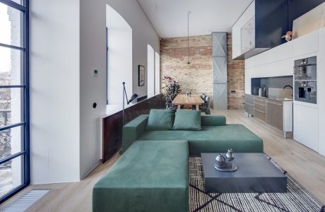 A modern, open-concept living space featuring exposed brick walls, a large sectional sofa, and integrated kitchen.