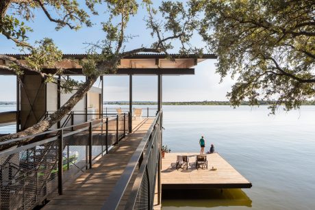 A modern wooden dock with a covered pavilion overlooking a tranquil lake surrounded by trees.