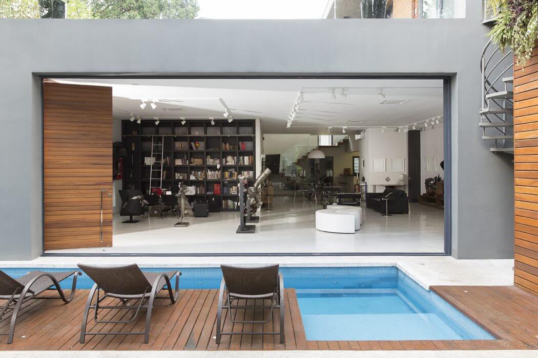 Modern open-concept house with pool, wooden deck, and glass wall exposing interior.