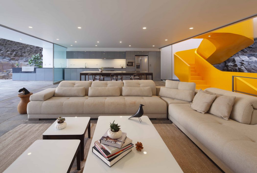 Spacious living area with modular beige sofas, wooden coffee tables, and an eye-catching yellow spiral staircase.