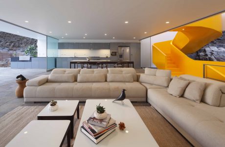 Spacious living area with modular beige sofas, wooden coffee tables, and an eye-catching yellow spiral staircase.