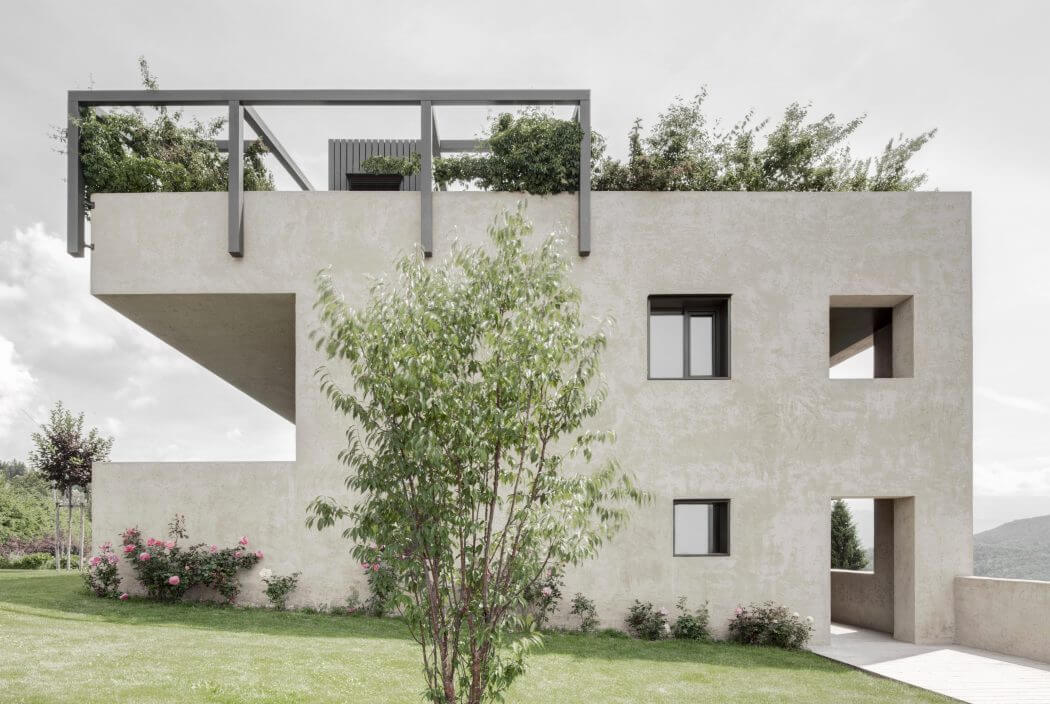 Modern concrete building with glass windows, cantilevered balconies, and lush landscaping.