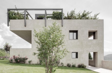 Modern concrete building with glass windows, cantilevered balconies, and lush landscaping.