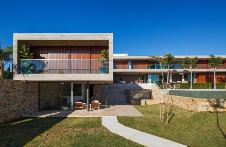 Modern beachside villa with timber-clad facade, expansive terrace, and lush landscaping.