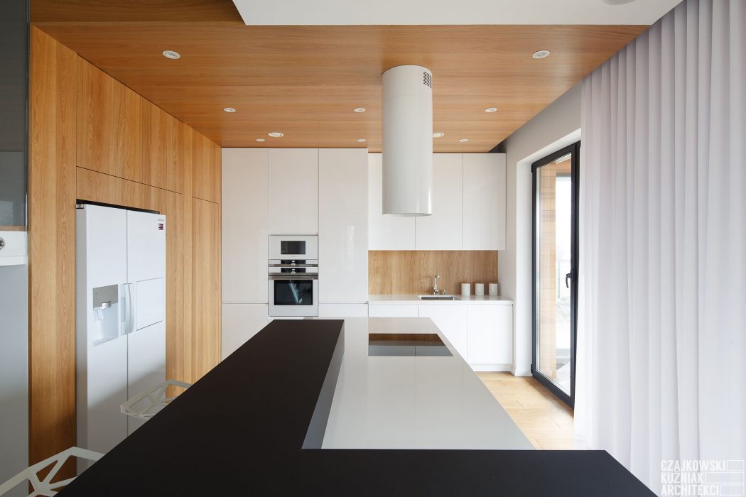 Modern kitchen with sleek white cabinets, wood accents, and a large black island countertop.
