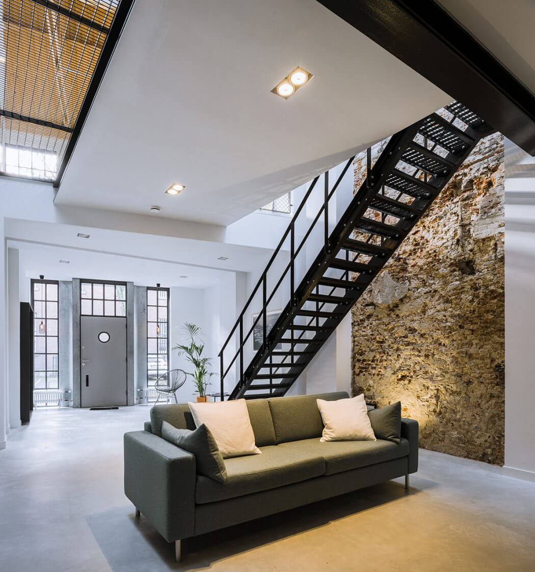 Sleek modern loft design with exposed industrial staircase and stone wall feature.