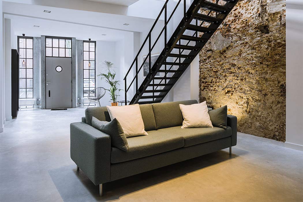 Sleek modern loft design with exposed industrial staircase and stone wall feature.