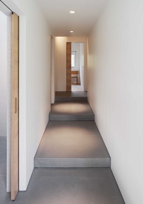 Minimalist hallway with concrete steps and subtle lighting, leading to a wooden doorway.