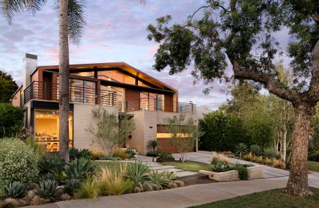 Modern home with wooden siding, floor-to-ceiling windows, and lush landscaping.