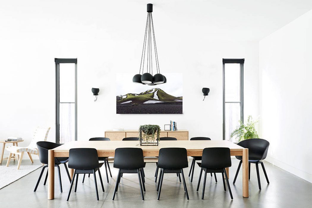 Modern dining room with wooden table, black chairs, and minimalist pendant lighting. Landscape artwork creates focal point.