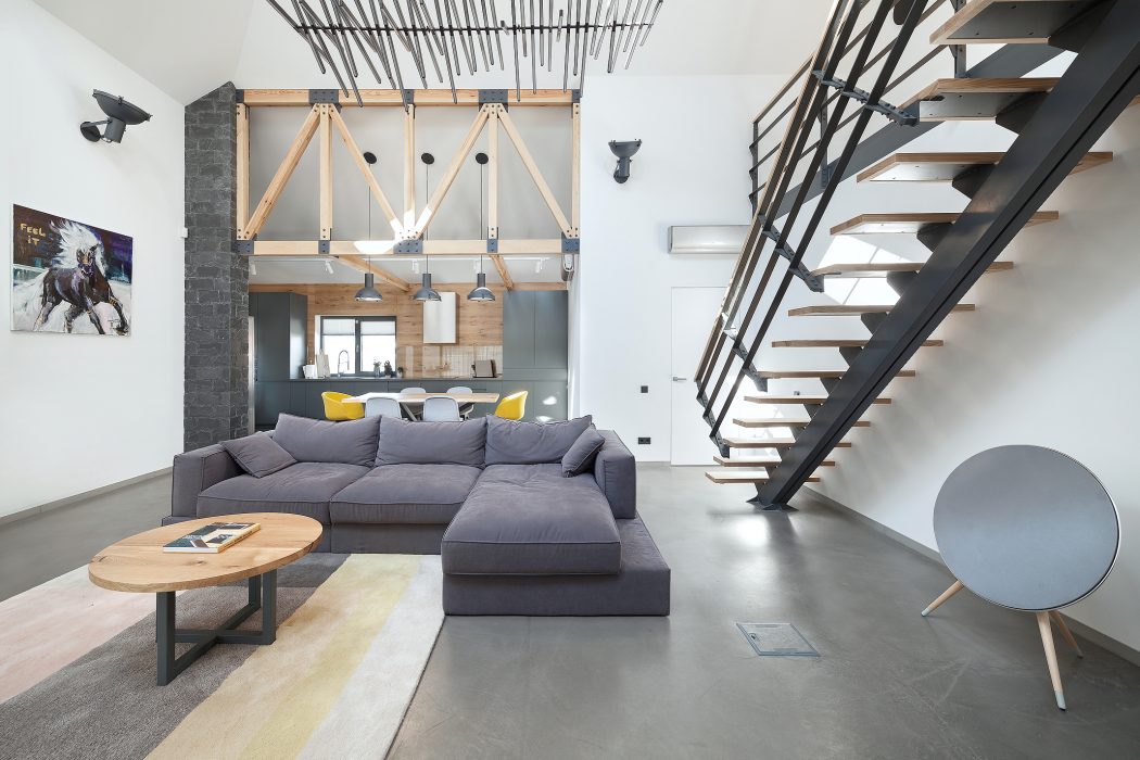 Spacious loft with exposed wooden beams, sleek black staircase, and cozy gray sectional sofa.
