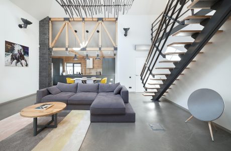 Spacious loft with exposed wooden beams, sleek black staircase, and cozy gray sectional sofa.