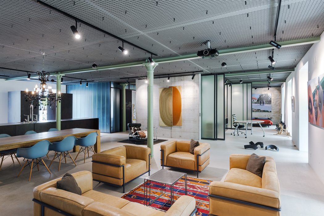 Modern, open-concept office with industrial-style lighting, bold artwork, and cozy lounge area.