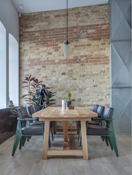 Rustic dining space with exposed brick wall, wooden table, and green upholstered chairs.