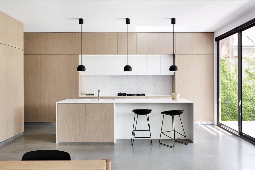 Sleek, minimalist kitchen with light wood cabinetry, white countertops, and pendant lighting.