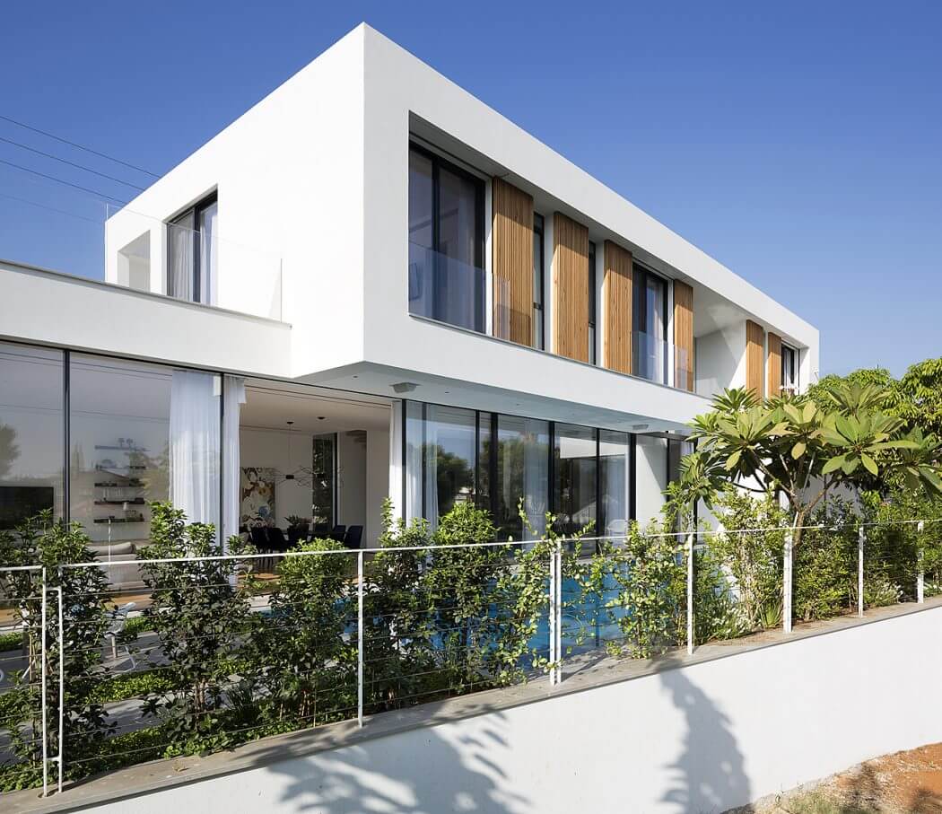 Modern, minimalist architecture with large glass windows, wooden shutters, and lush greenery.