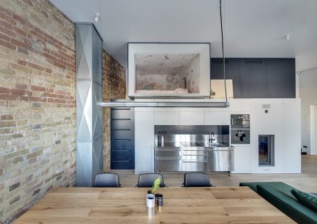 A modern kitchen with stainless steel appliances, brick walls, and a wooden dining table.