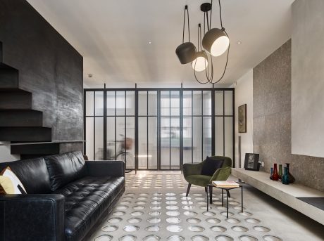 Modern, minimalist living space with black leather sofa, green armchair, and patterned flooring.