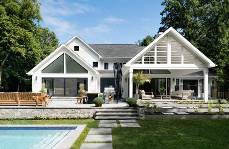 Large white house with gabled roof, wrap-around porch, and modern outdoor entertaining area.