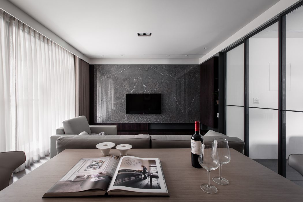 Elegant living room with sleek gray marble wall, modern furniture, and a wine setup on the table.