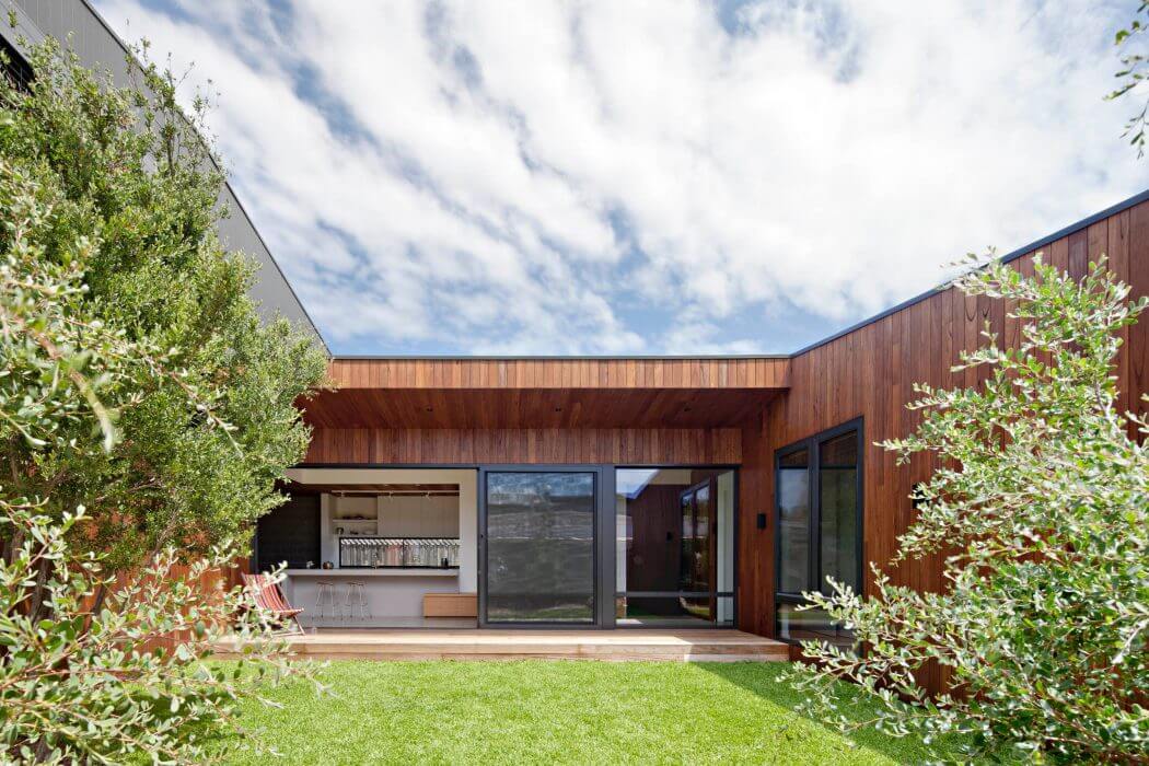 Modern wood-paneled home with large windows, patio, and lush landscaping.
