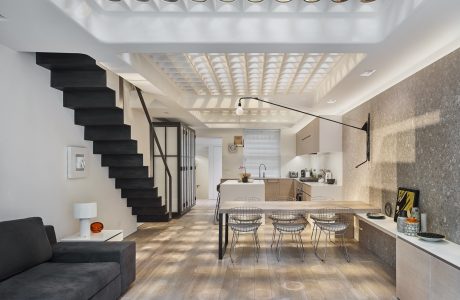 Modern open-concept kitchen and dining area with sleek black stairs, industrial lighting, and wood floors.